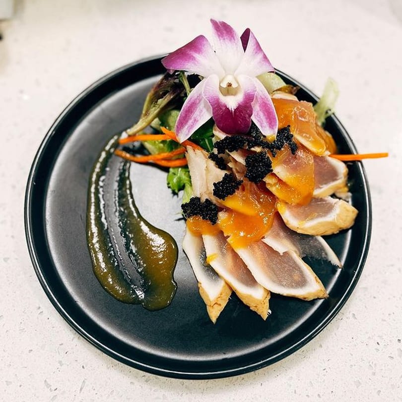 Japanese seared tuna sashimi with caviar, orange sauce, and an orchid on a black plate.