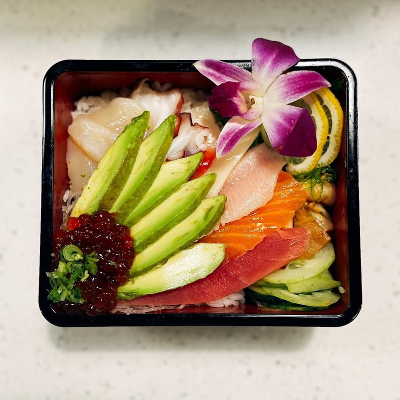 A colorful chirashi bowl from Soi Bistro, featuring various sashimi, avocado, and a purple orchid.