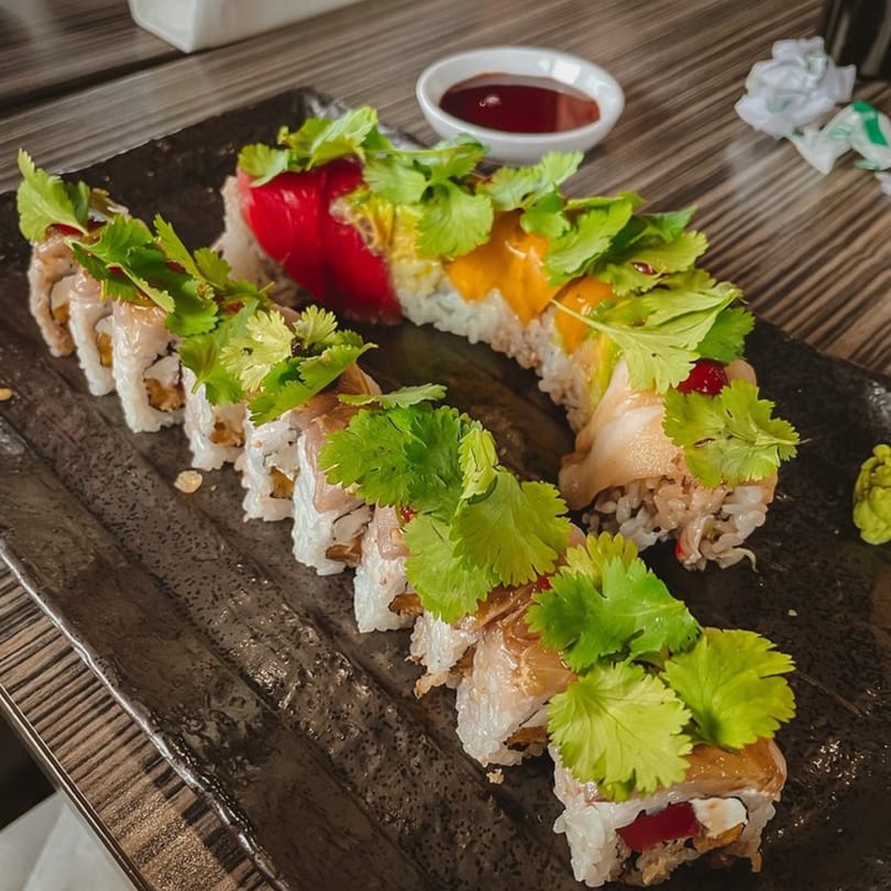 Soi Bistro's colorful sushi rolls with cilantro, red and yellow toppings, and soy sauce.