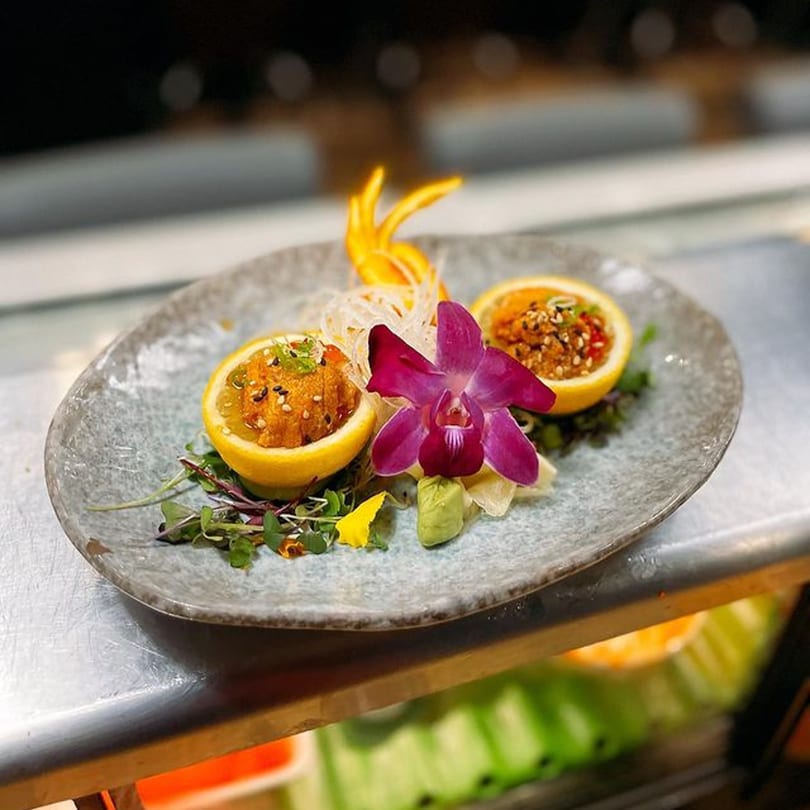 Soi Bistro's uni served in lemon halves with microgreens, wasabi, and an orchid on a grey plate.