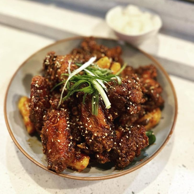 Soi Bistro's crispy fried chicken wings, glazed with sauce, sesame seeds, and green onions.